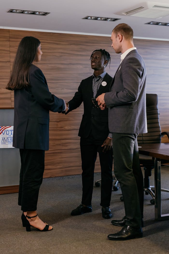 Three professionals in a conference room handshake during a business meeting.